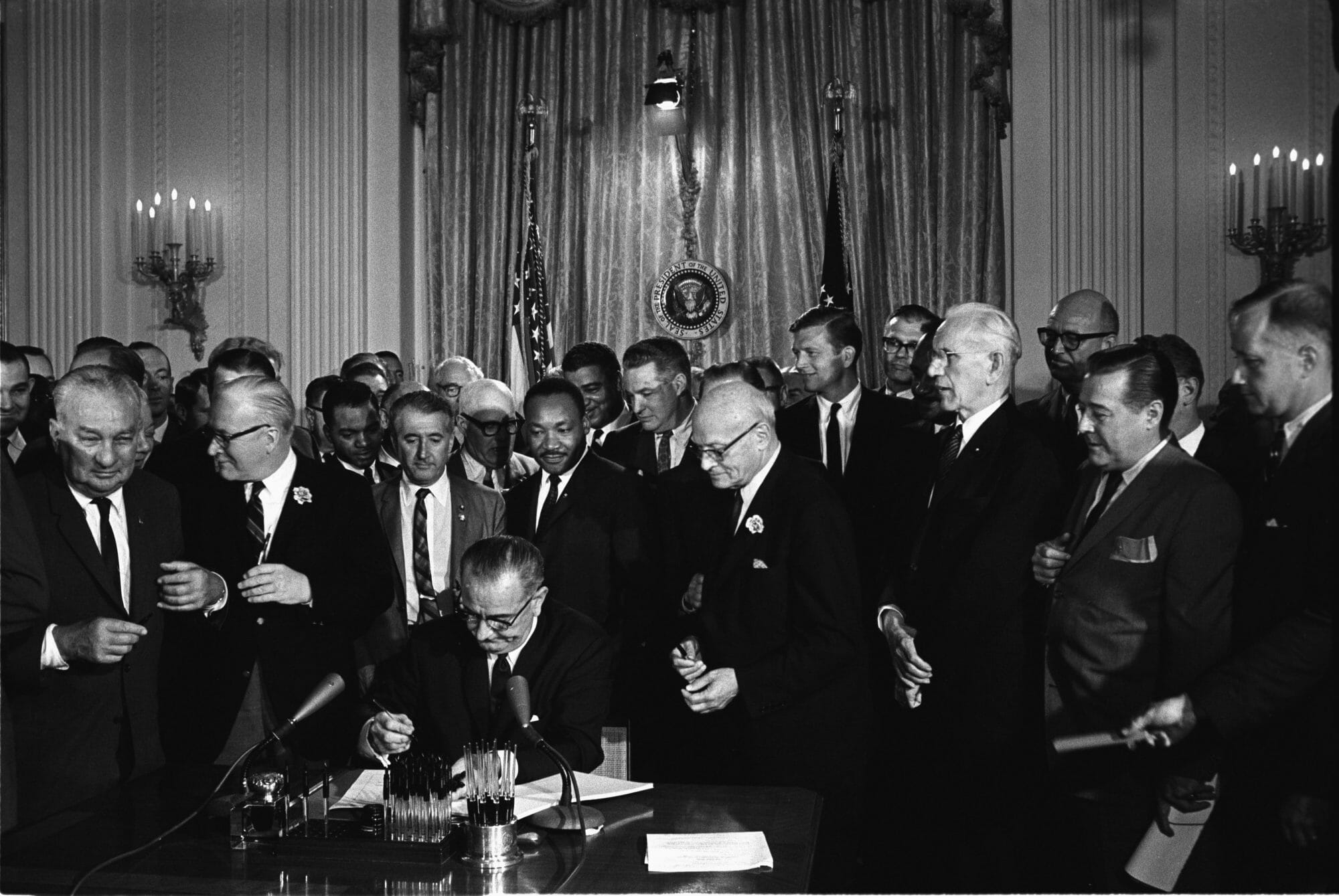 Cecil Stoughton, "President Lyndon B. Johnson signs the 1964 Civil Rights Act as Martin Luther King, Jr., and others, look on," Photograph, July 2, 1964. Wikimedia Commons, https://en.wikipedia.org/wiki/File:Lyndon_Johnson_signing_Civil_Rights_Act,_July_2,_1964.jpg. 
